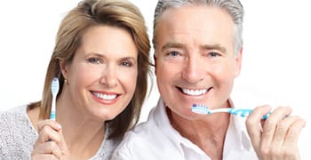 An older couple smiling while holding toothbrushes.