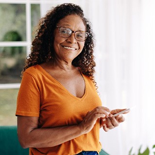 Senior woman with glasses smiling while looking at phone