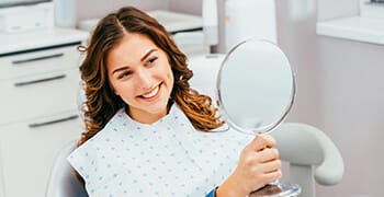 Woman examining smile in hand-held mirror