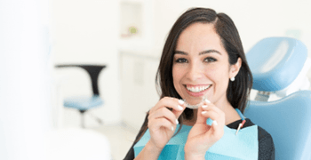 Woman smiling while holding Invisalign aligners