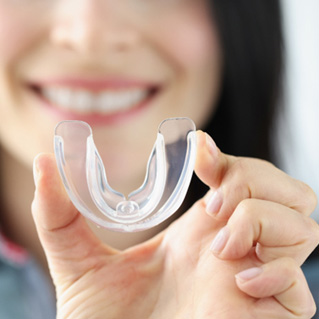 A smiling woman holding up a transparent plastic mouthguard
