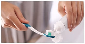 Hands putting toothpaste on toothbrush