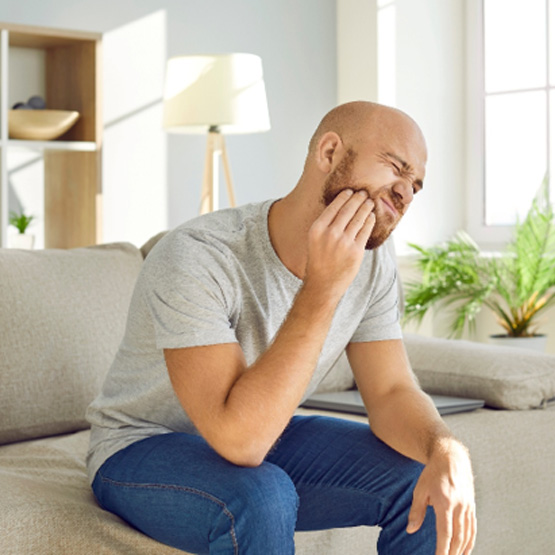 Man on couch squinting touching hand to jaw in pain