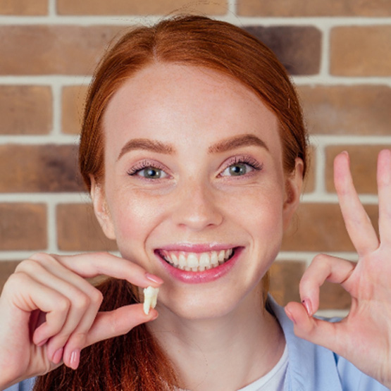 Woman holding extracted tooth and making “ok” sign with other hand