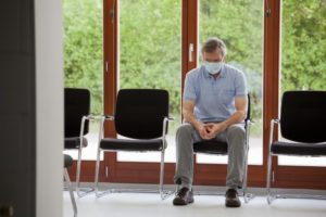 older man wearing face mask and sitting in waiting room 